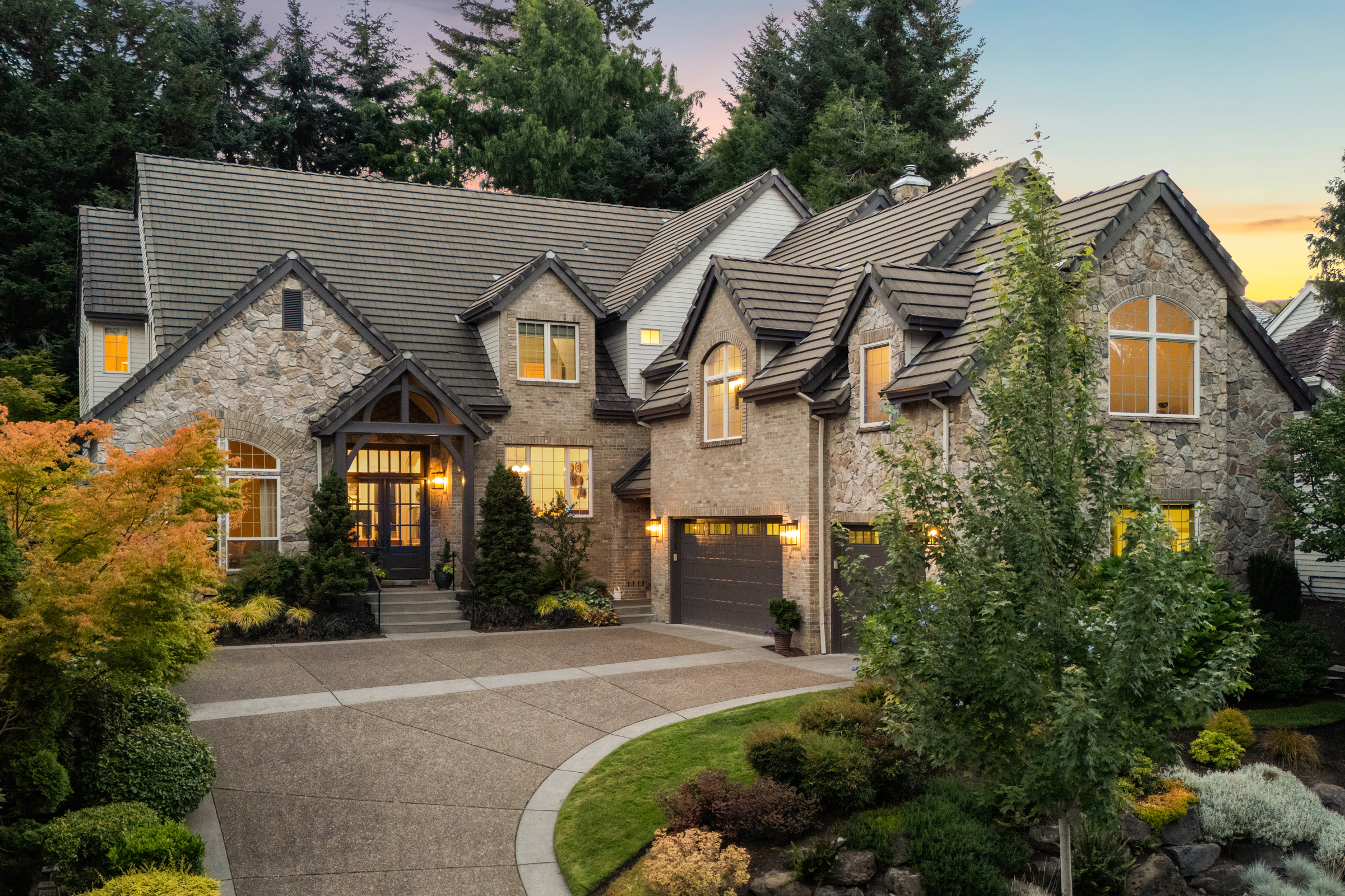 Stone-front home surrounded by trees at dusk